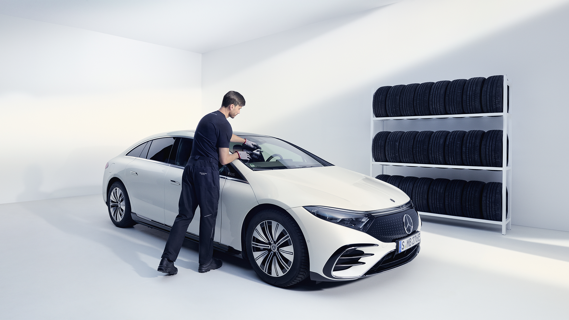Mercedes-Benz-mekaanikko korjaamassa valkoisen Mercedes EQS:n tuulilasia.