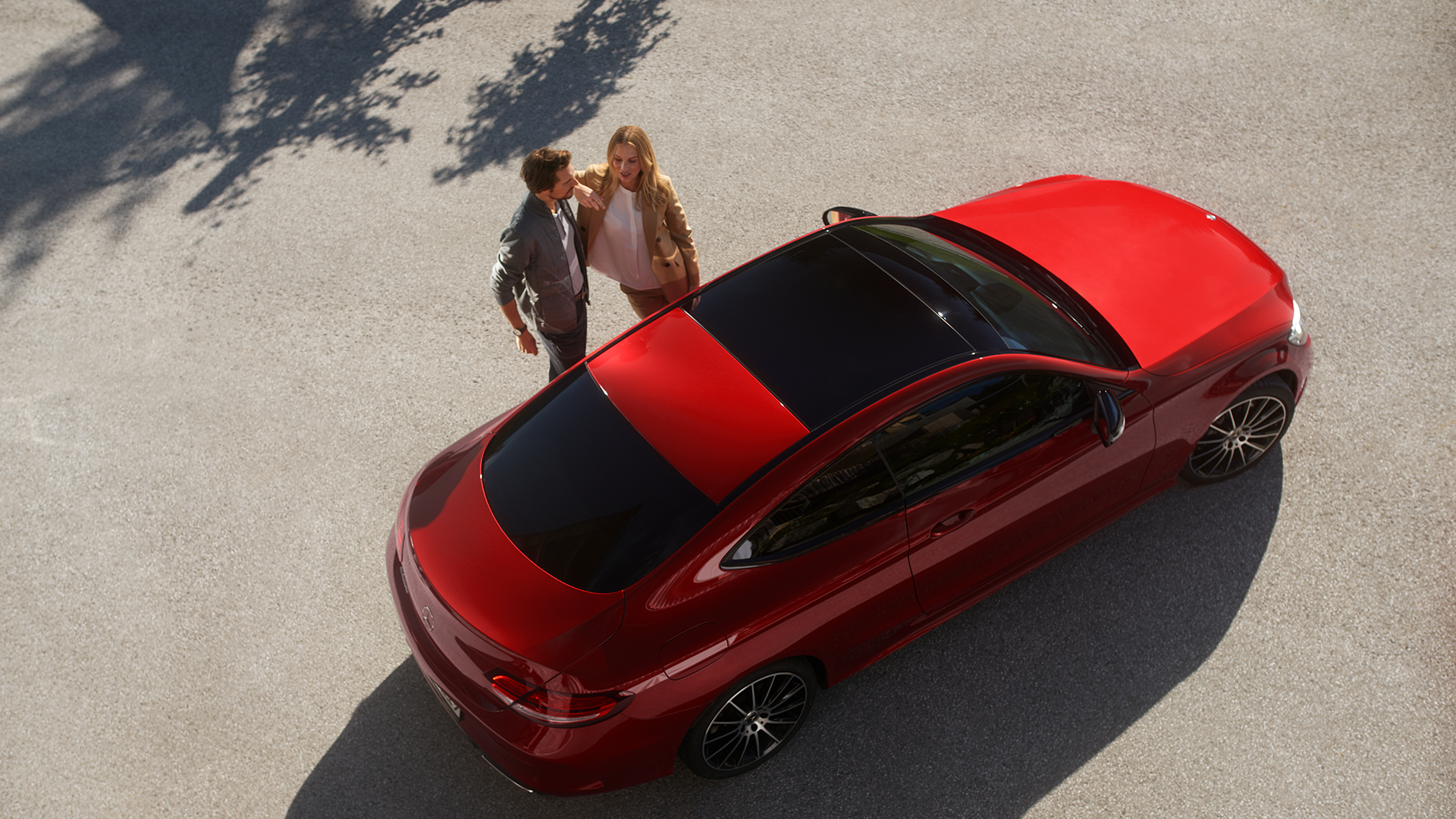 Pariskunta yhdessä kirkkaan punaisen Mercedeksen vieressä auringonpaisteessa.